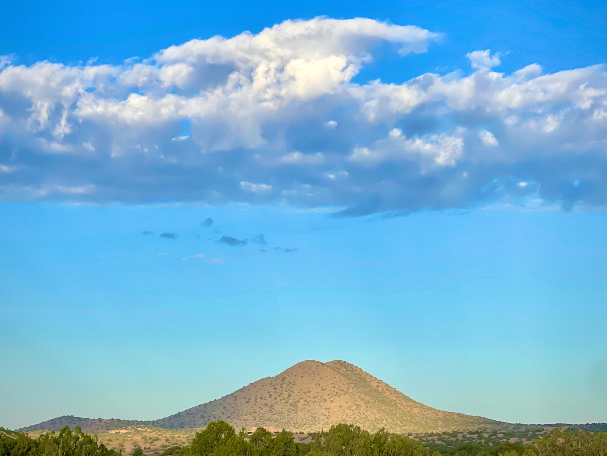 photograph of a Cerrillos Hill splashed in sunlight as a long white cloud hovers above the peak against deep blue sky